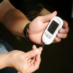 A person checking their blood glucose level using a blood glucose meter, with a small drop of blood on their fingertip and the device displaying the measurement.